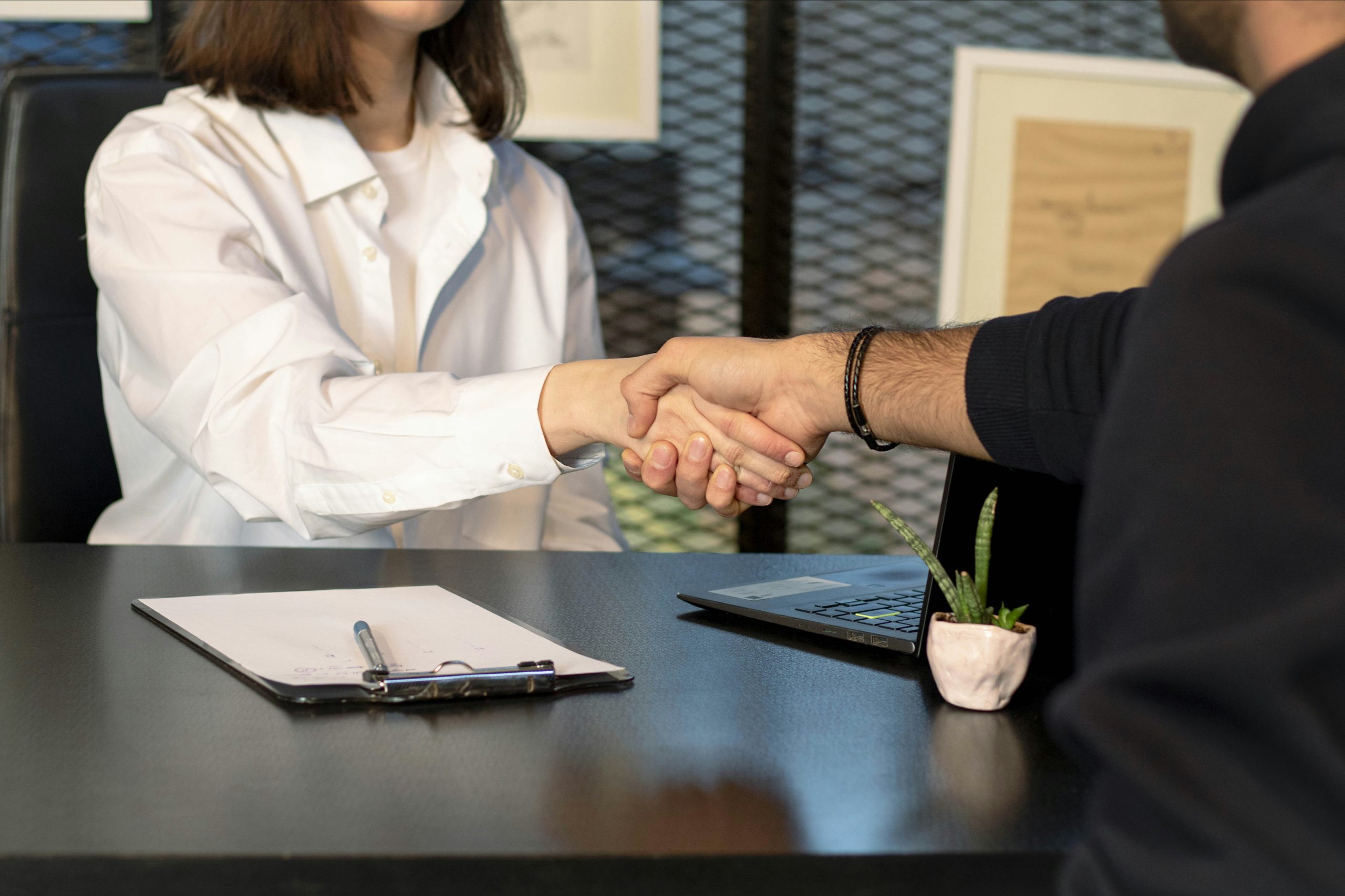 Hands engaged in negotiation across a modern office desk, symbolizing the importance of structural flexibility and custom markups in optimizing IB commission structures.