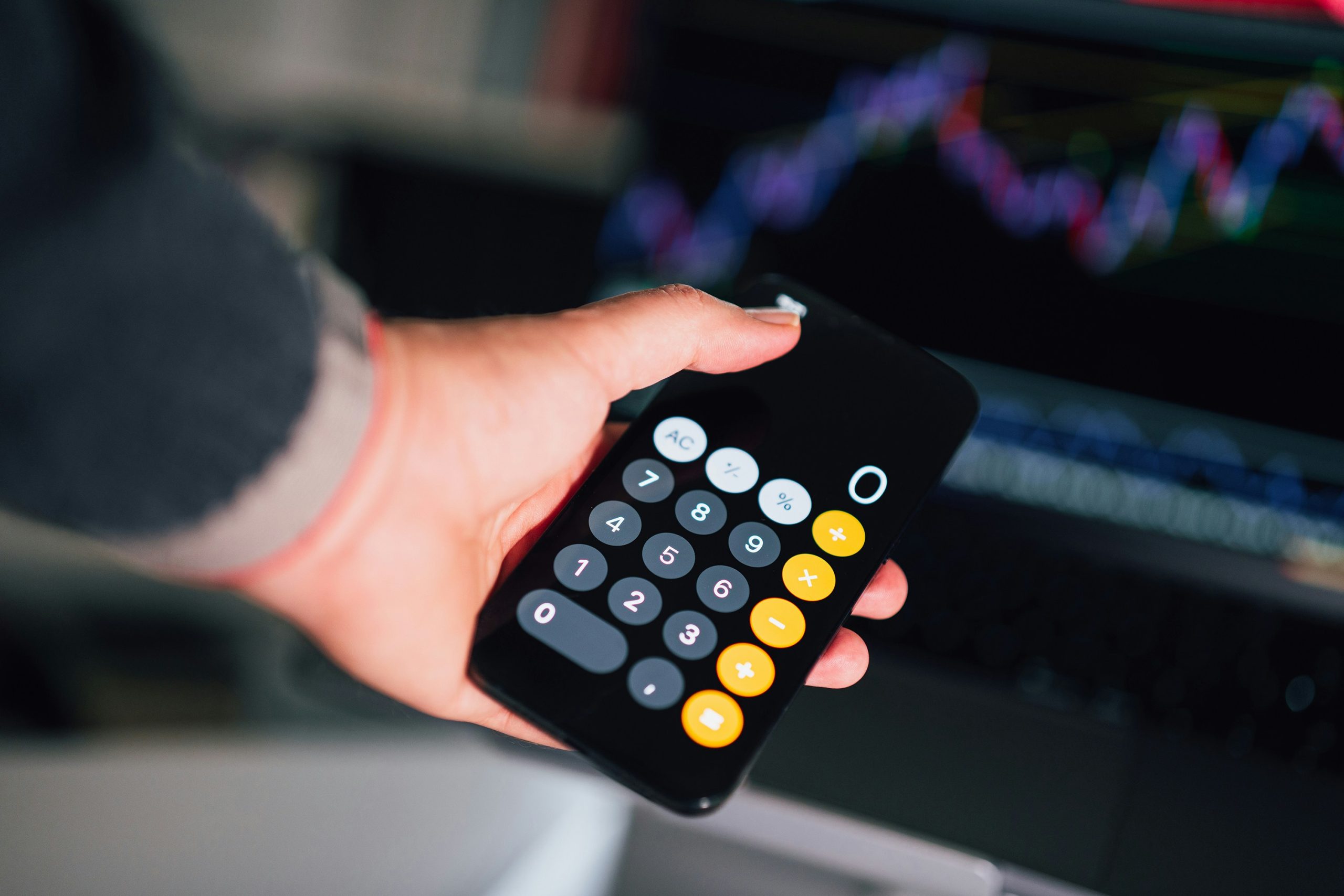 A person's hand pressing buttons on a calculator with blurred currency in the background, symbolizing the monetization and high rebates gained from automated trading volumes.